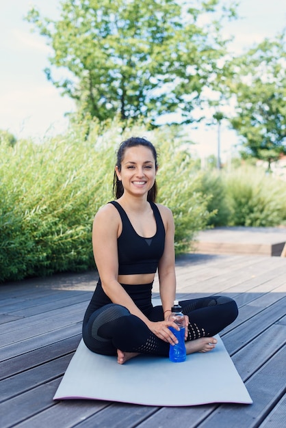 Sportieve jonge vrouw maakt yoga oefenen met yogamat in het park buiten actieve levensstijl concept