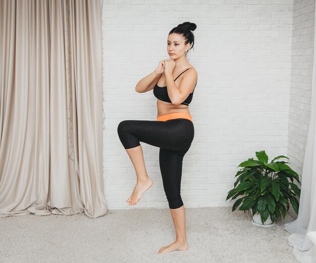 Sportieve jonge vrouw traint thuis. slank meisje, gaat sporten op een thuisfitnessmat, hurkt met haar handen.