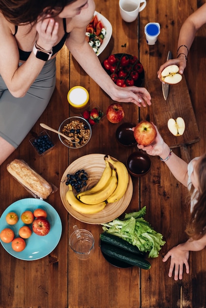 Sportieve jonge vrouwen aan de keukentafel met groenten en fruit.