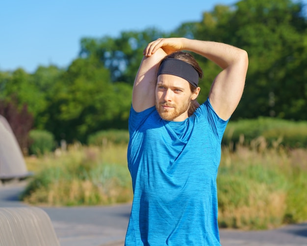 Sportieve jongeman in sportkleding opwarmen in de natuur op zonnige dag