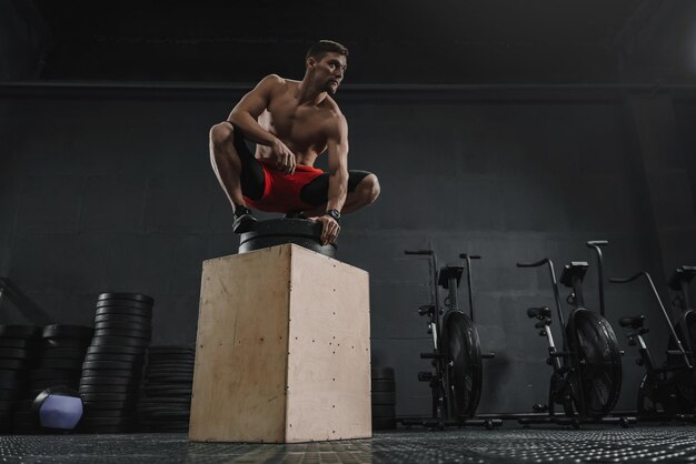 Sportieve jongeman rust na box jump oefening in de sportschool