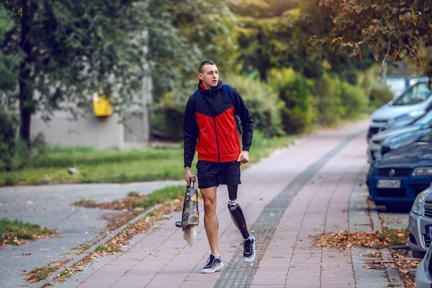 Sportieve Kaukasische gehandicapte man met kunstbeen, in sportkleding en rugzak op straat lopen. In handen is kunstbeen.