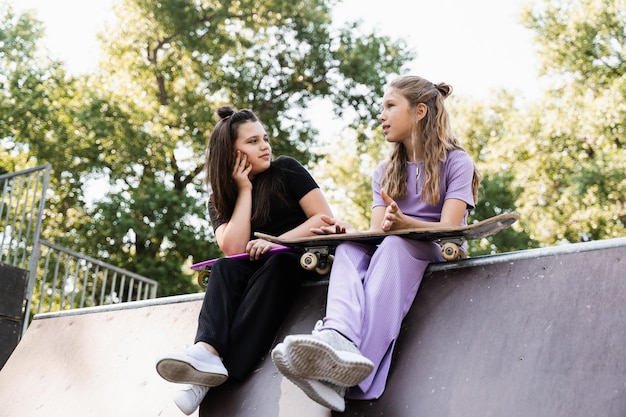 Sportieve kinderen meisjes met skateboard en penny boards zitten en chatten met elkaar op sporthelling op speelplaats Vrienden communicatie en vriendschap Sport extreme levensstijl