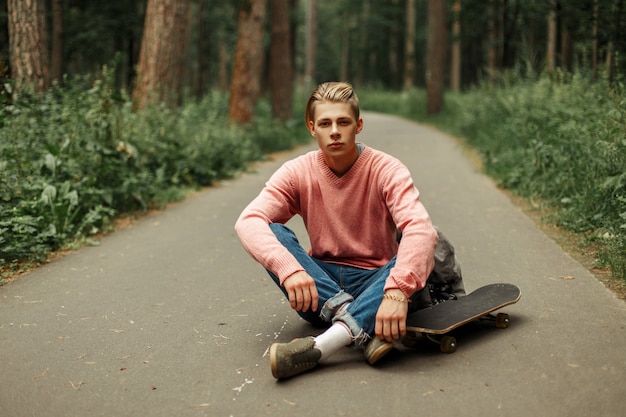 Sportieve knappe jongeman met skateboard en rugzak zittend op het asfalt