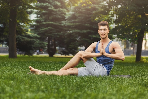 Sportieve man die yoga beoefent, zittend op het gras in het park. Jonge man mediterend met gesloten ogen, namaste op groen gras in park, kopieer ruimte