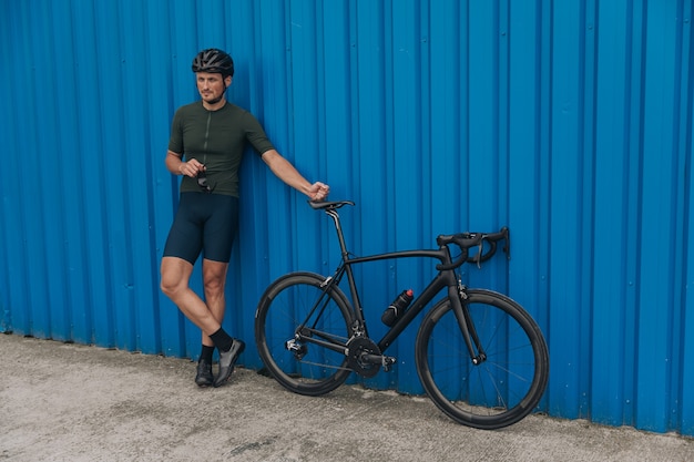 Sportieve man in helm staande in de buurt van zwarte fiets buitenshuis