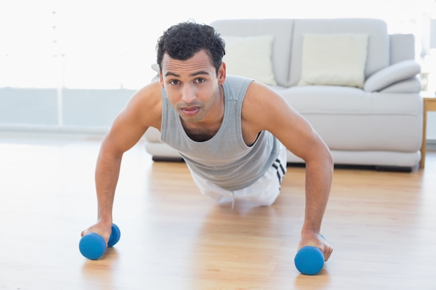 Sportieve man met halters doen push-ups in de woonkamer