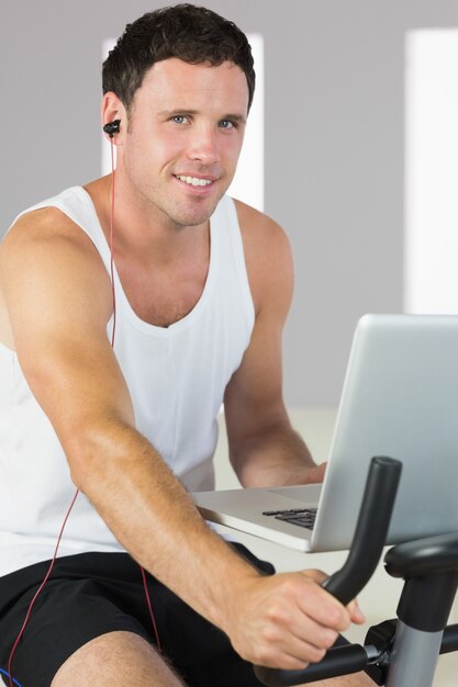Sportieve man met oortelefoons te oefenen op de fiets, die laptop en lachend