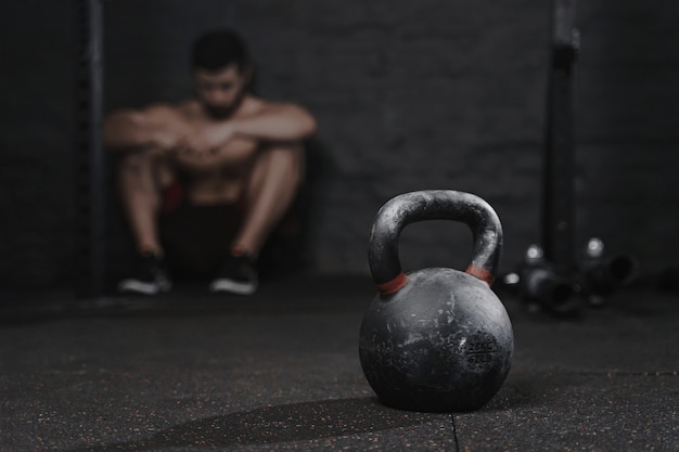 Sportieve man zit op de sportschool te lijden aan instorting te overwinnen. Demotivatie sport concept. Stress en vermoeidheid bij het sporten. Crossfit kettlebell training.