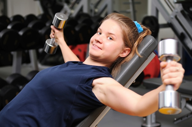 Sportieve meisje in sportkleding liggend op fitnessapparatuur training met halters op sportschool