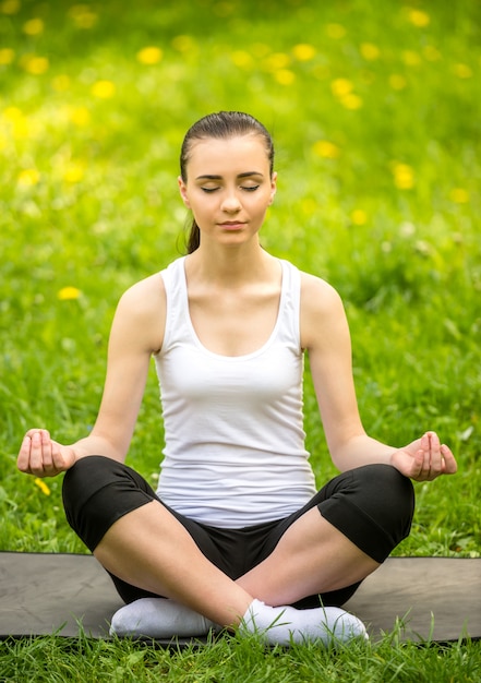 Sportieve meisjeszitting op de mat in de zomerpark en het doen van yoga