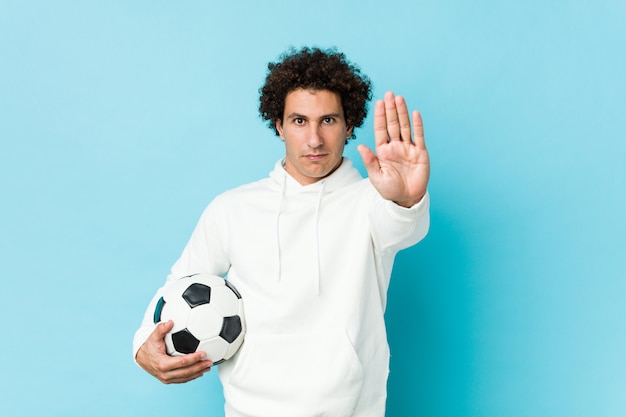 Sportieve mens die een voetbalbal houdt die zich met uitgestrekte hand bevindt die eindeteken toont, dat u verhindert.