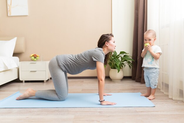 Sportieve mooie zwangere moeder met zoontje oefenen op blauwe yogamat