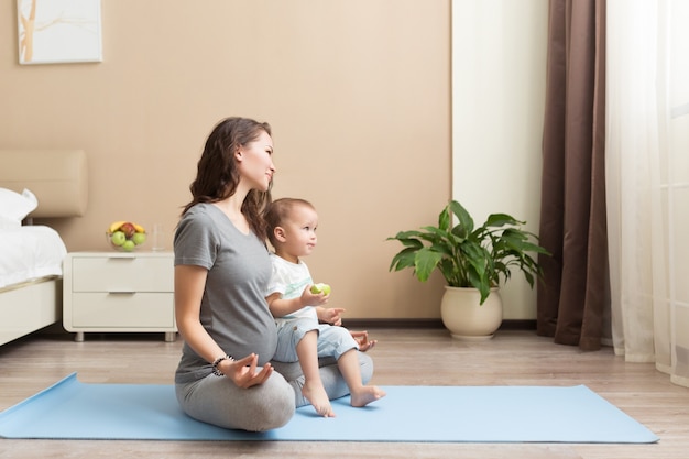 Sportieve mooie zwangere moeder met zoontje oefenen op blauwe yogamat