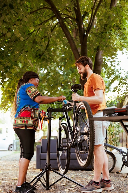 Sportieve vriend en vriendin repareren fietsschade in achtertuin met behulp van professionele reparatiestandaard en gereedschap. Actief jong multiraciaal stel dat de fiets vasthoudt en vastzet voor onderhoud.
