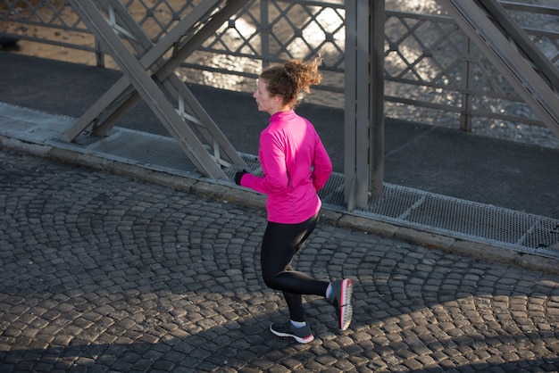 sportieve vrouw die op de stoep loopt tijdens het joggen in de vroege ochtend met zonsopgang in de stad op de achtergrond