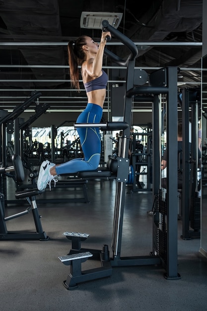 Sportieve vrouw die traint op geassisteerde pullup-machines in de sportschool