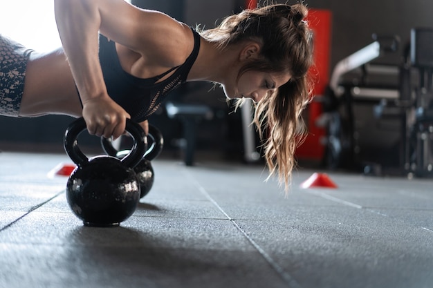 Sportieve vrouw doet push-ups in de sportschool met kettlebells