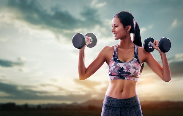 Sportieve vrouw houdt fitness dumbbell vast met een glimlach die traint met de natuur en de berglucht op de achtergrond