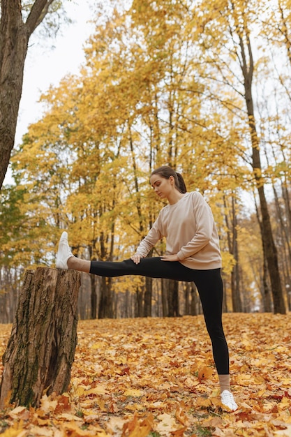 sportieve vrouw in activewear benen strekken in de buurt van boom en oefeningen doen