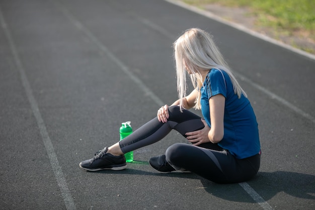 Sportieve vrouw met enkelblessure in atletiekbaan., Gezondheidszorg en sportconcept. groene bidon om te drinken