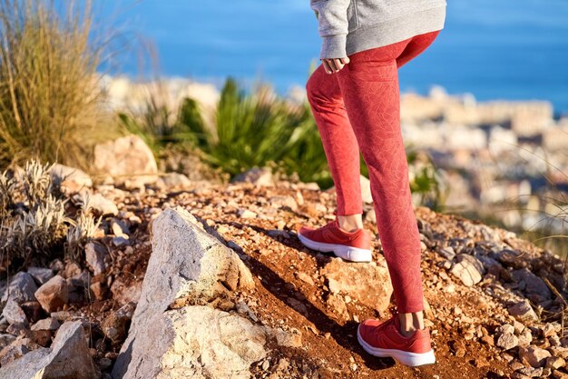 sportieve vrouw met lang haar en rode legging die uitkijkt op de zee vanaf de bergtop