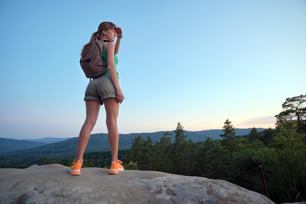 Sportieve vrouw staat alleen op heuvelpad vrouwelijke wandelaar geniet van uitzicht op de avond natuur vanaf rotsachtige klif op wildernispad actieve levensstijl concept