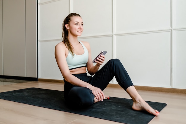 Sportieve vrouwenzitting op yogamat thuis met online telefoon