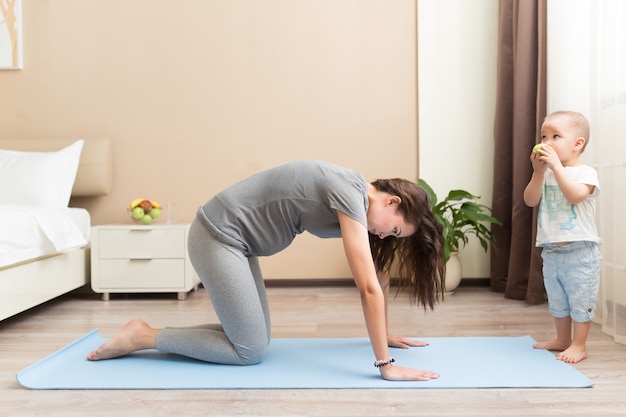 Sportive beautiful pregnant mother with baby son exercising on blue yoga mat