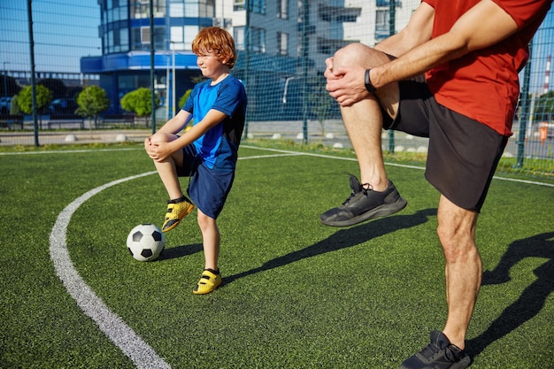 Foto padre e figlio sportivi che fanno esercizio fisico e si scaldano le gambe prima dell'allenamento di una partita di calcio allo stadio della città