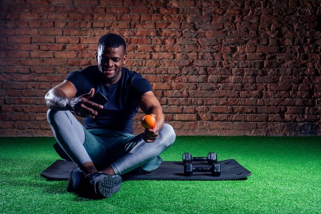 Sportive detox african american man resting after training with apple and smartphone in hand