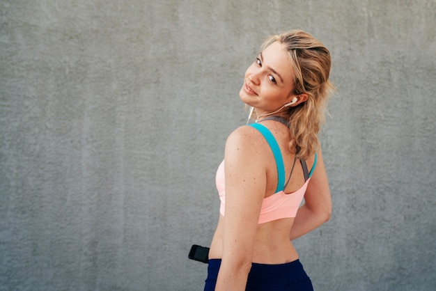 Sportive girl near the wall in headphones view from the back