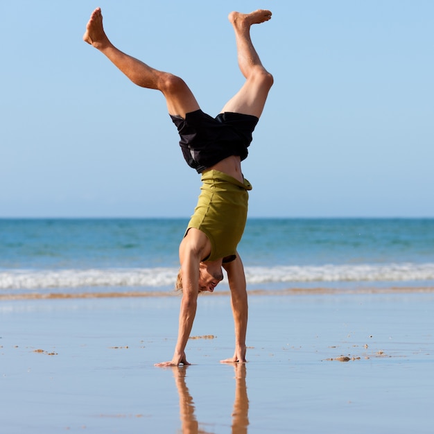 Uomo allegro che fa ginnastica sulla spiaggia