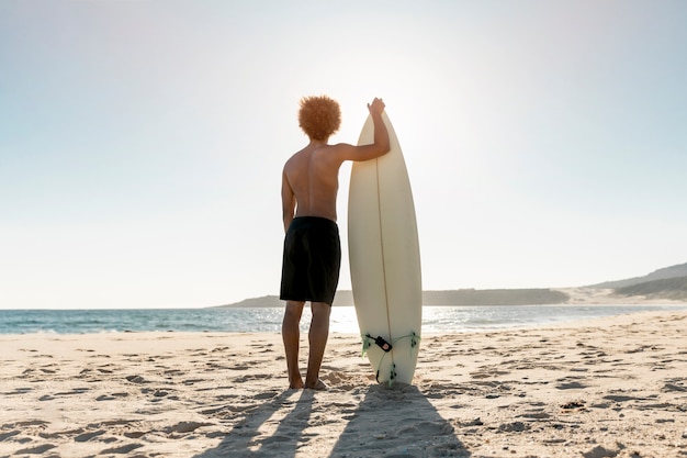 Спортивный человек, стоящий на берегу моря с доской для серфинга