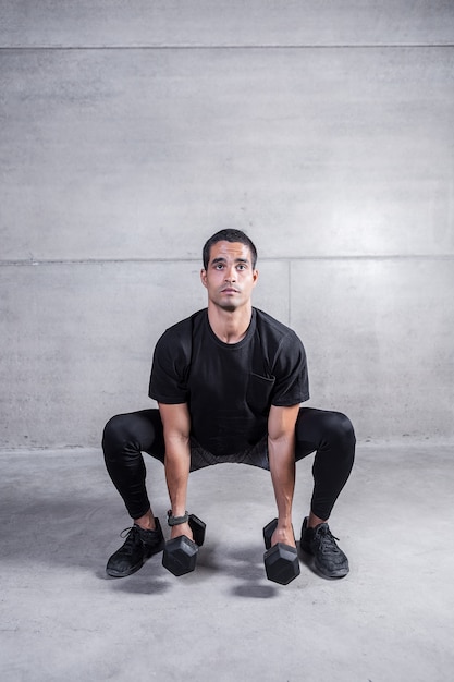 Sportive man with dumbbells in squat position