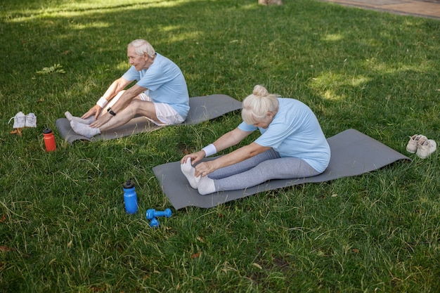 スポーツの成熟した家族のカップルは夏の日に公園に座って膝の練習をします