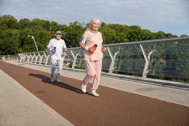 Photo sportive mature woman with friend in tracksuits run training together on modern footbridge