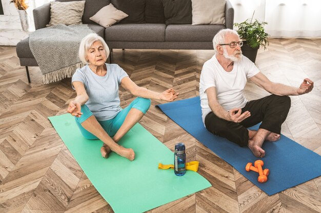 Coppia anziana sportiva che fa esercizi di fitness e rilassamento a casa - gli anziani si allenano per rimanere in salute e in forma