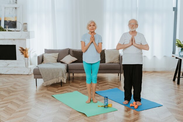 Sportive senior couple doing fitness and relaxation exercises at home - Elderly people training to stay healthy and fit