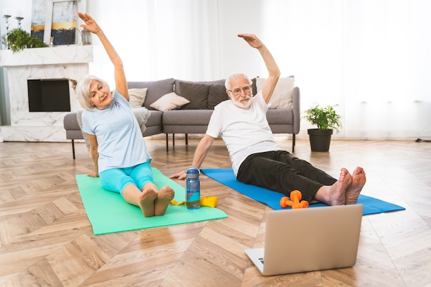 Sportive senior couple doing fitness and relaxation exercises at home - Elderly people training to stay healthy and fit