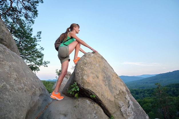 Sportive woman climbing alone on hillside rocky trail Female hiker overcoming difficult cliff on wilderness path Active lifestyle concept