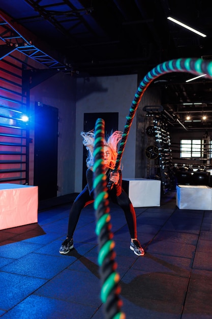 A sportive woman does exercises using sports equipment - rope, goes in for sports in the gym.