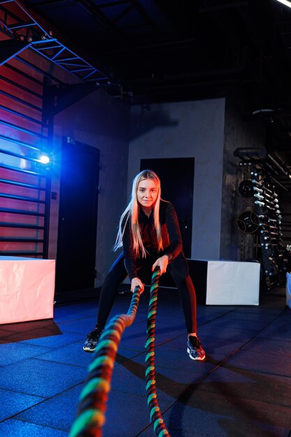 A sportive woman does exercises using sports equipment - rope, goes in for sports in the gym.