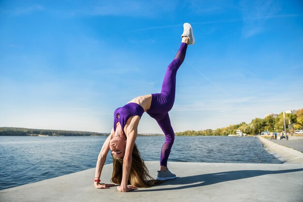 Sportive woman doing yoga exercise in the park, near the lake at daytime. Healthy lifestyle concept