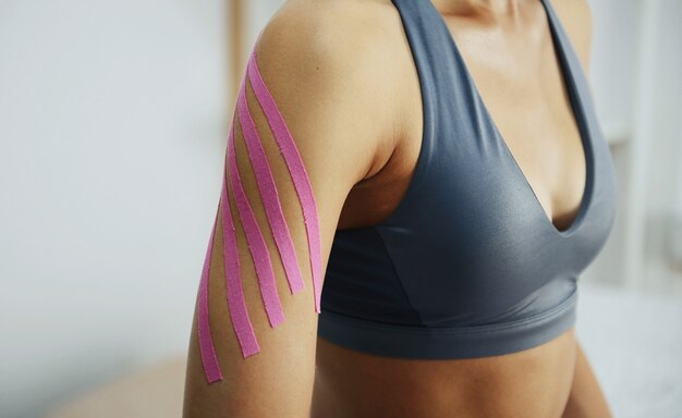 Photo sportive woman sits indoors with kinesio tape on her hand.