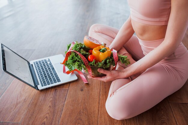 Foto donna sportiva seduta sul tavolo con laptop e cibo sano.