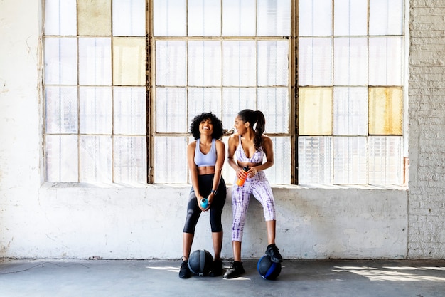 Photo sportive women talking in a gym while drinking water