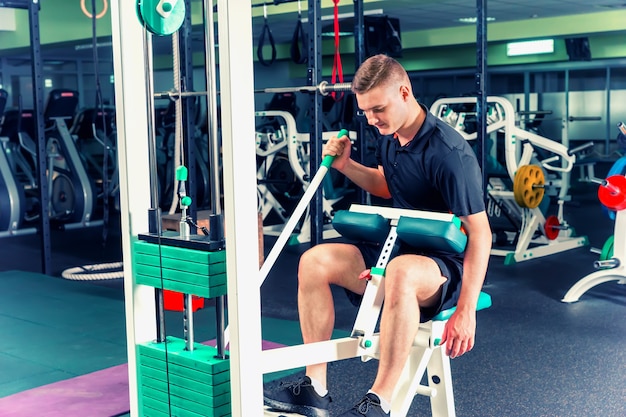 Sportive young man in sportswear doing exercise on a machine looking focused