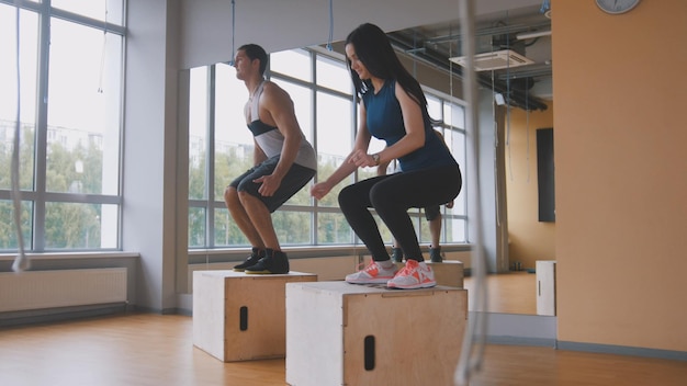 Sportive young woman and muscular man fitness instructor doing box jump exercise during a workout at.