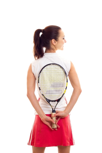 Спортивная молодая женщина в белой спортивной рубашке и красной юбке с темным хвостиком держит теннисную ракетку